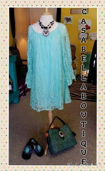 Turquoise embellished dress displayed with black heels and matching handbag in a boutique setting