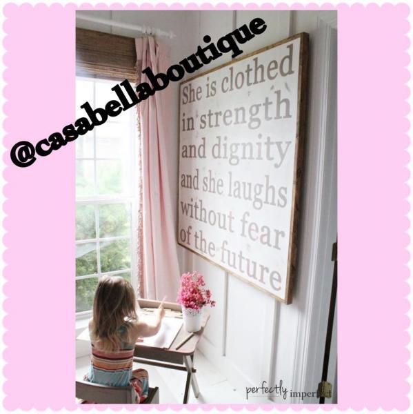 Child painting at a desk beside a framed Bible verse on a white wall in a sunlit room