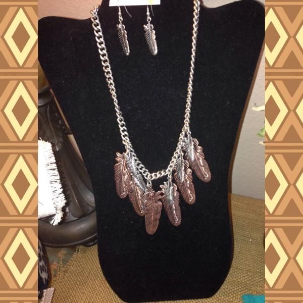 Black velvet display bust with silver chain necklaces and feather-shaped pendants against patterned wallpaper