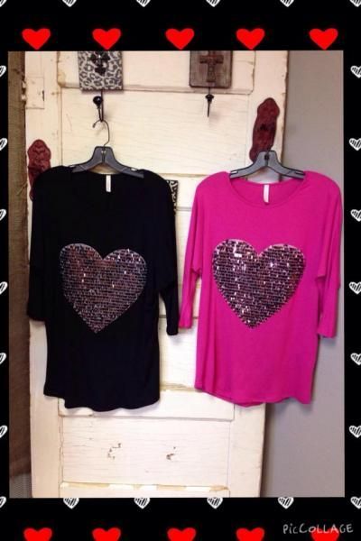 Two heart-decorated tops, one black and one pink, hanging on hooks against a white wall