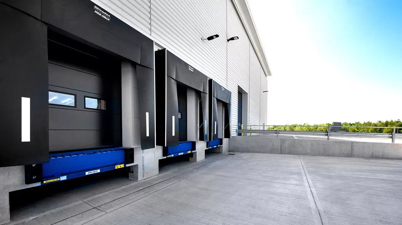 Row of black loading dock doors beside a concrete yard under bright daylight