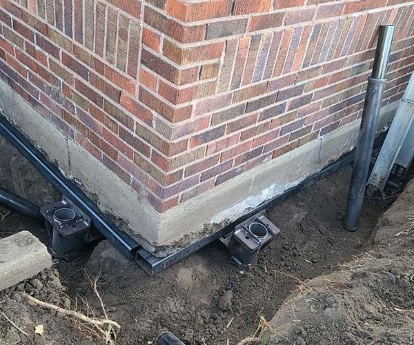 Brick house corner with foundation drainage pipes and exposed dirt around the base