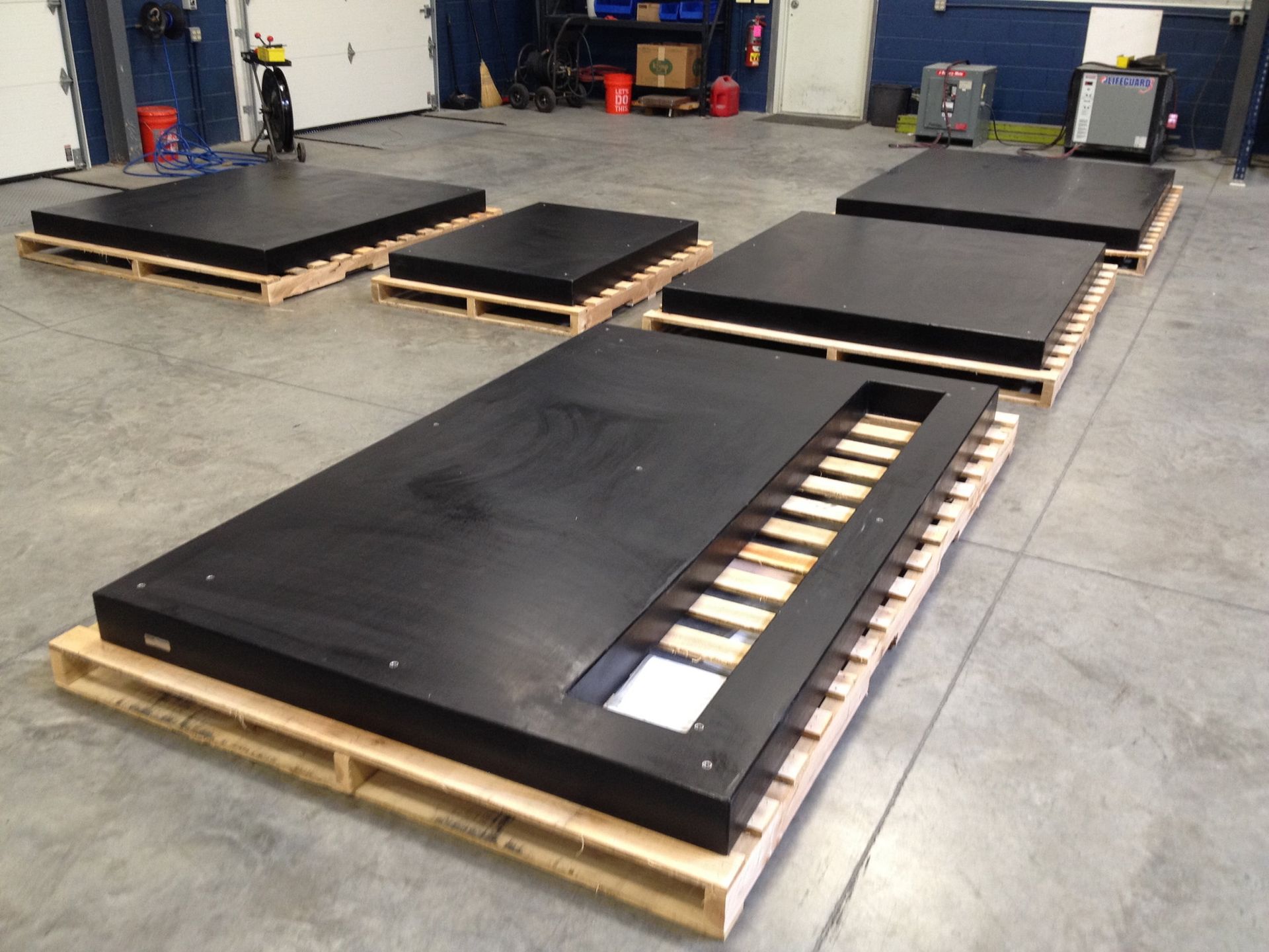 Black modular platform pieces on wooden pallets in a workshop or warehouse.