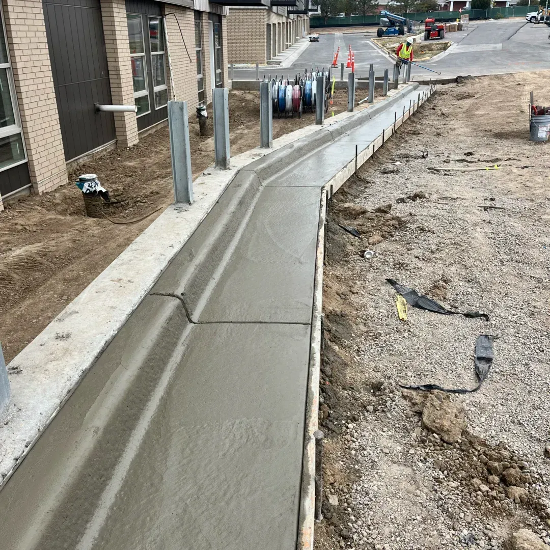 New concrete sidewalk beside a building and construction area with bollards and exposed dirt