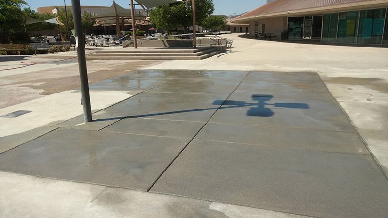 Concrete courtyard with a painted blue directional marking between low buildings and poles.