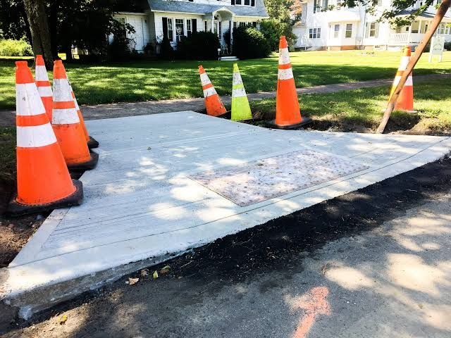 Orange traffic cones around a newly poured concrete sidewalk at a residential curb