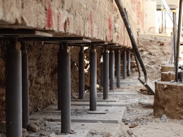Construction site with concrete pillars supporting an elevated structure over a rough dirt trench.