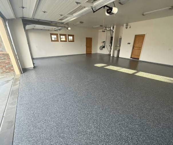 Empty garage with gray epoxy floor, white walls, two doors, and exercise equipment along the back wall