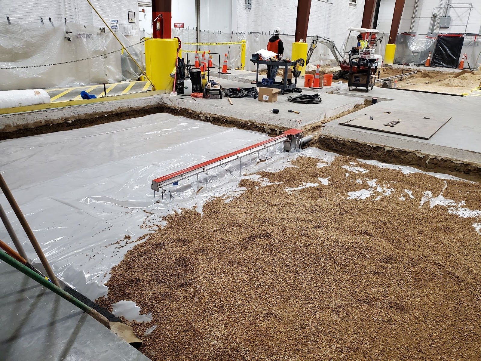 Construction site with workers, plastic-covered floor, and gravel spread in the foreground