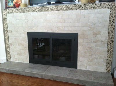 Fireplace with light tile surround, dark metal fireplace insert, and wood log border.
