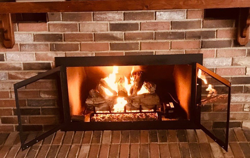 Fireplace with burning wood, brick surround, and open glass doors.