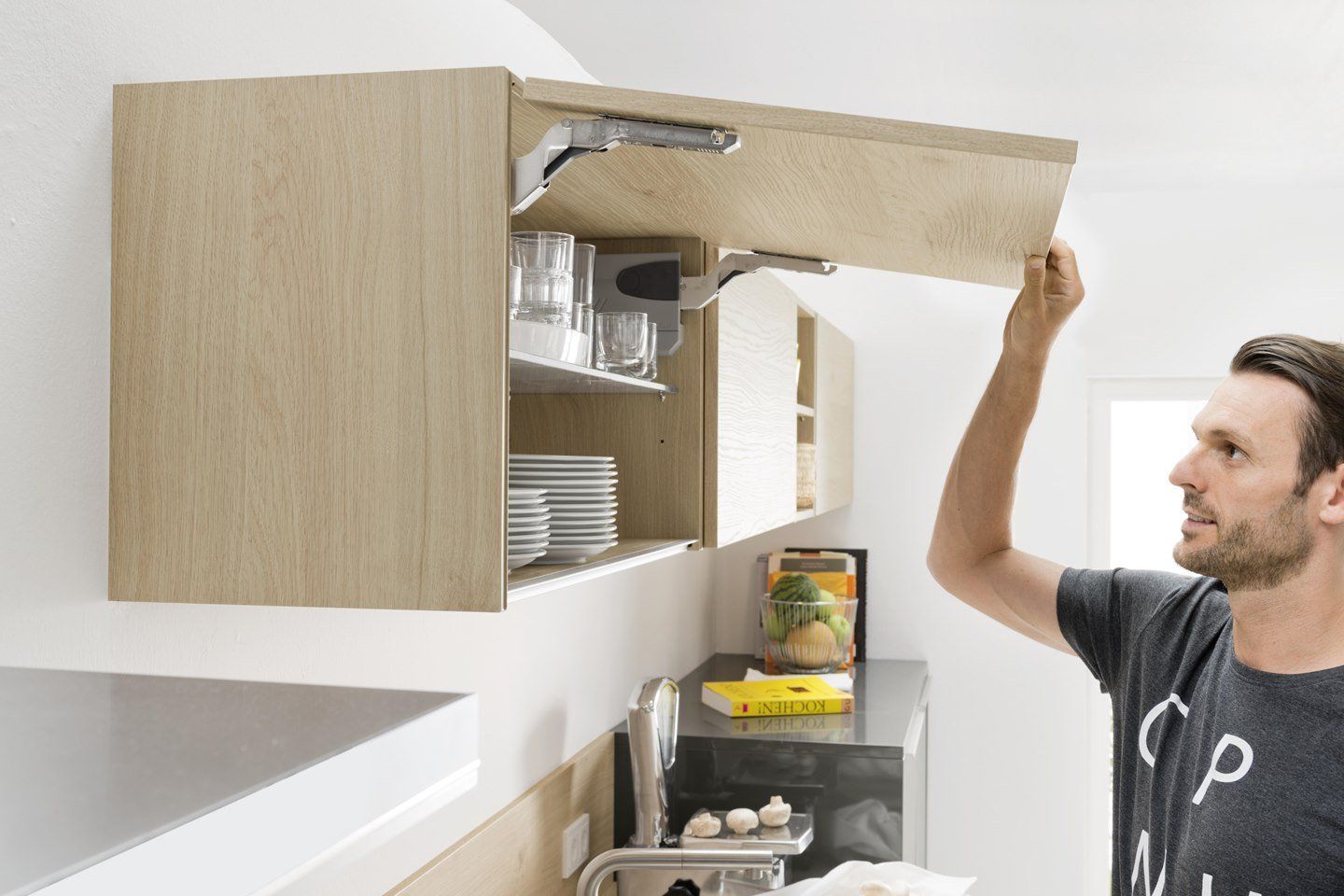 Un homme ouvre un placard en bois dans une cuisine