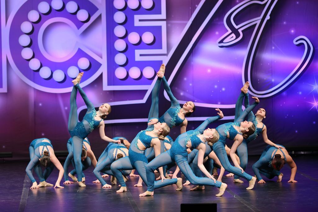 Gymnasts in blue costumes pose in a pyramid on a purple-lit stage with large CE6 letters in back