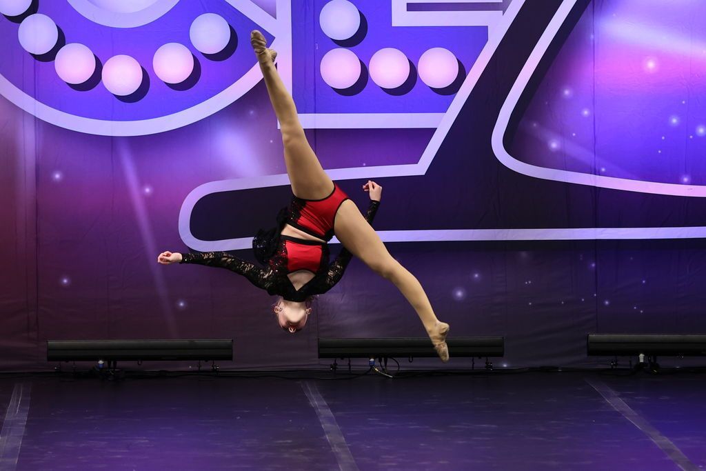 Gymnast mid-air in a split leap on a purple-lit stage with geometric backdrop