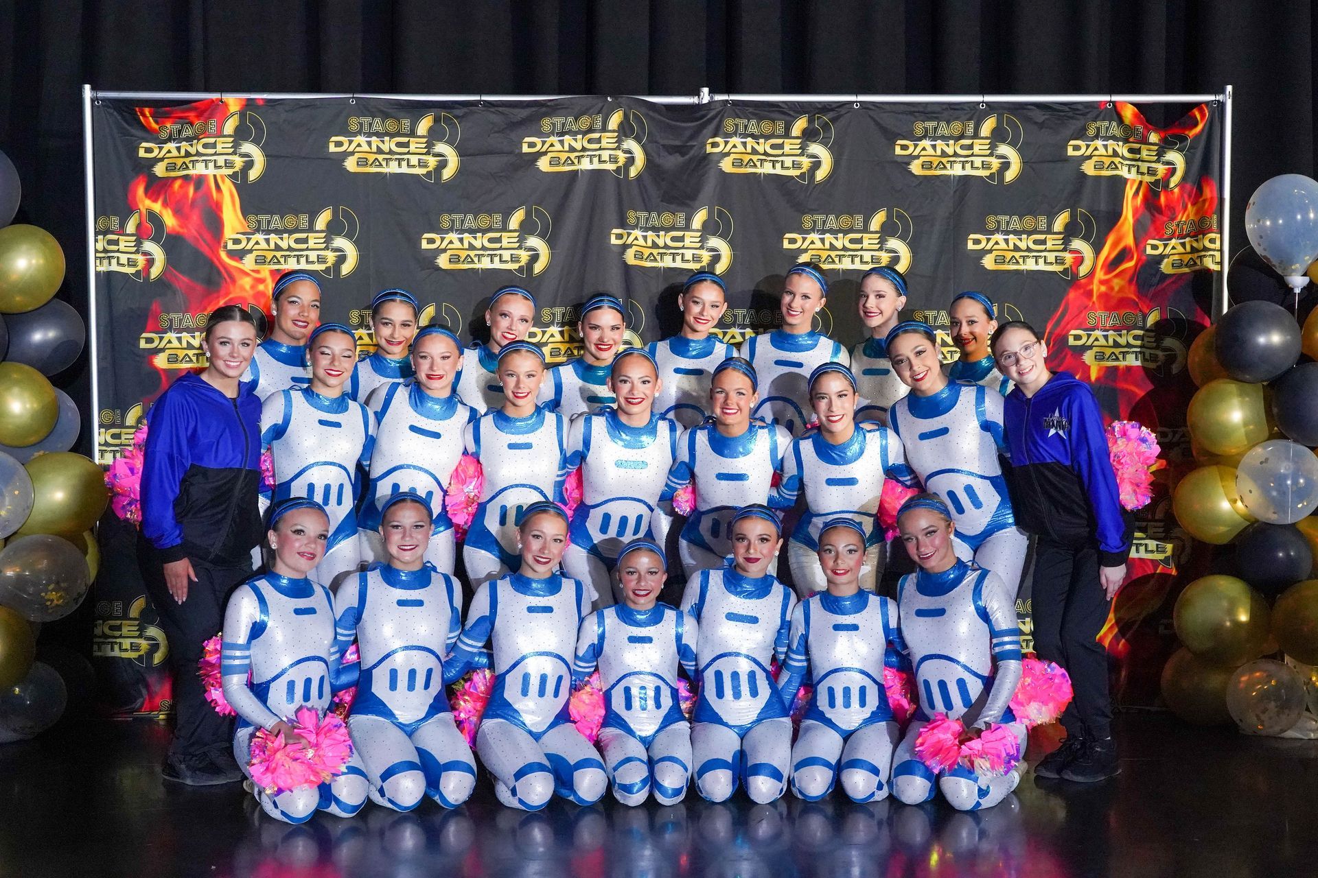 Youth sports team posing in blue-and-white uniforms at a sponsor backdrop with balloons and medals