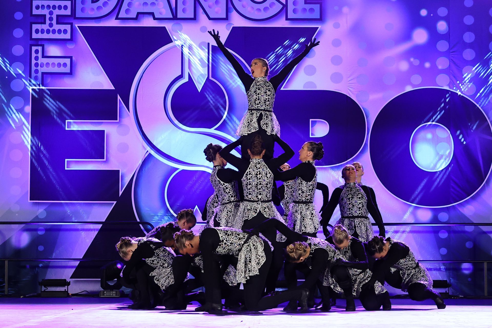 Dance team performing a pyramid on a purple-lit stage with large “EPO” letters in the background