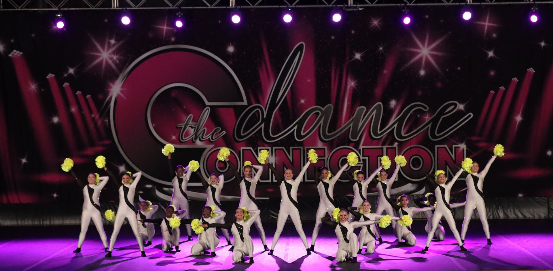 Dance team performing on a purple-lit stage with a large “Galactic” backdrop and neon costumes.