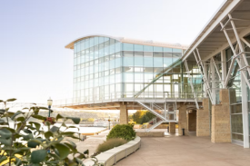 Modern glass building with curved facade and covered walkway on a waterfront campus