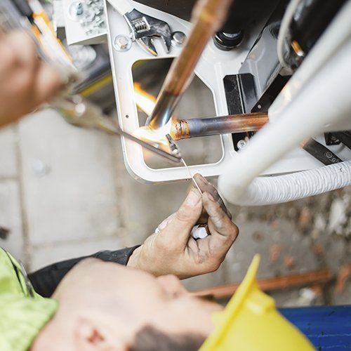 Tecnico che salda tubi di rame all'interno di un'unità HVAC esterna, con scintille visibili.