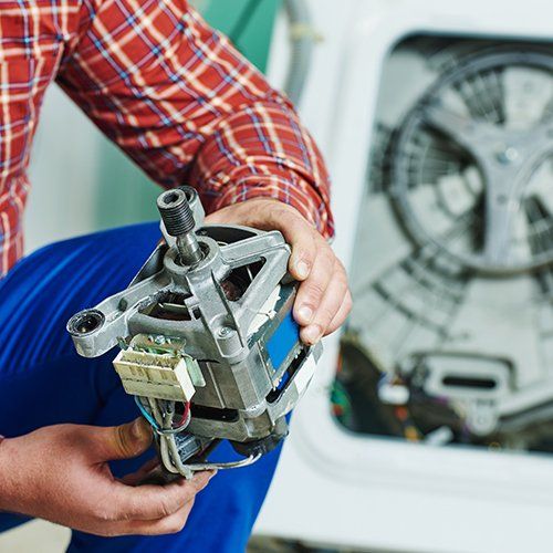 Un tecnico tiene in mano il motore di una lavatrice davanti a un elettrodomestico smontato.