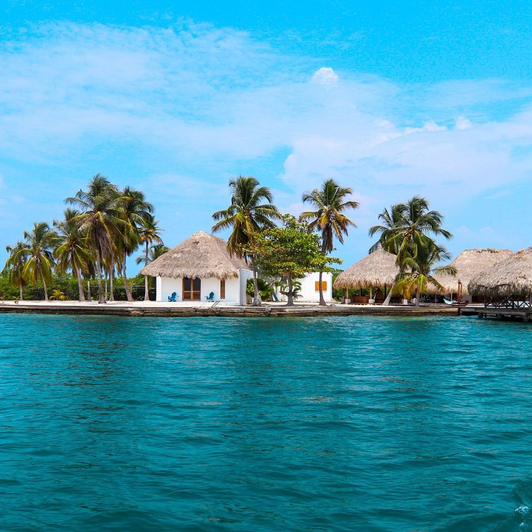 Thatched-roof cabins in the Islas de San Bernardo surrounded by palm trees, trees, and the sea