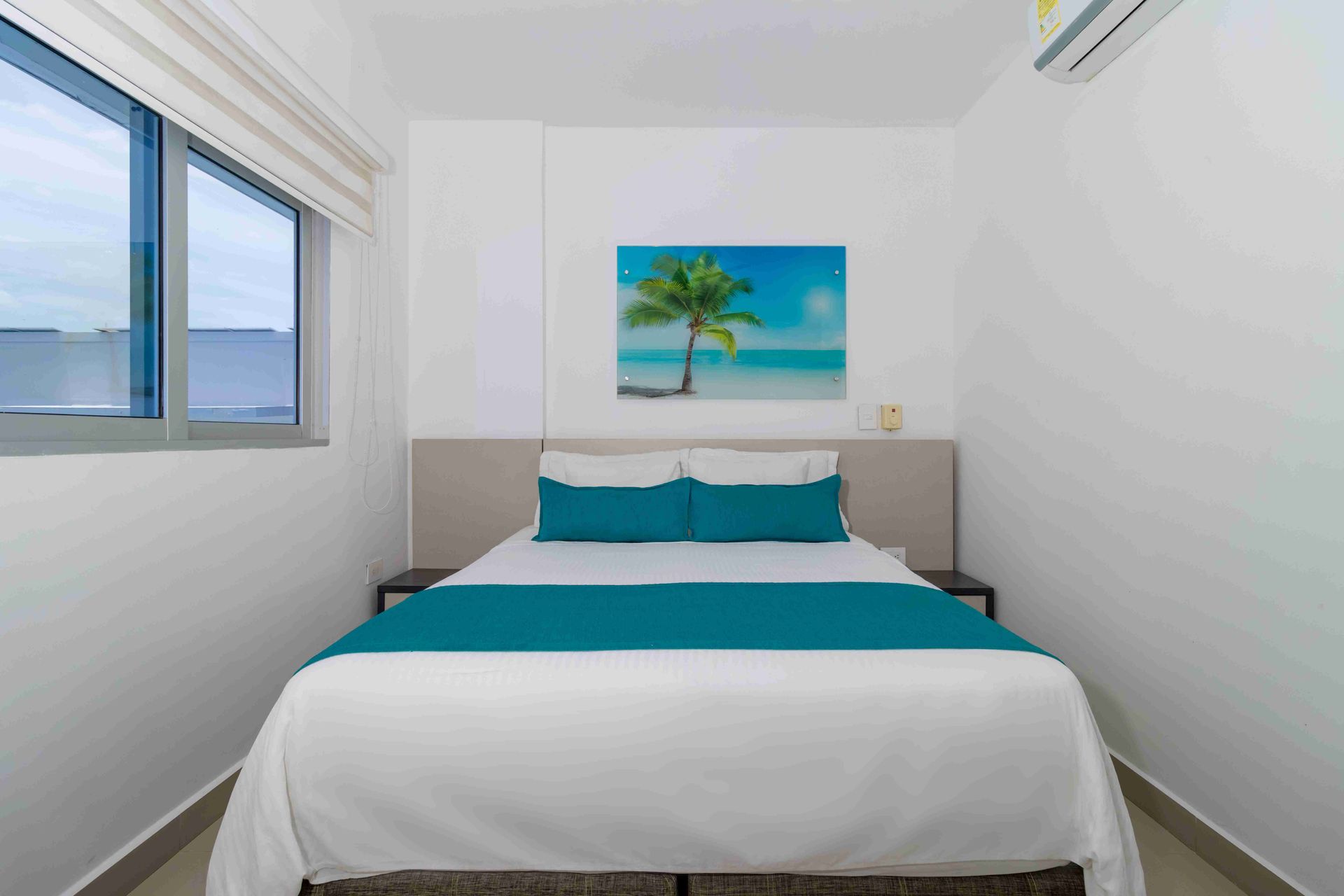 habitaciones en coveñas de Hotel Poblado con cama matrimonial, aire acondicionado y cuadro de palmera