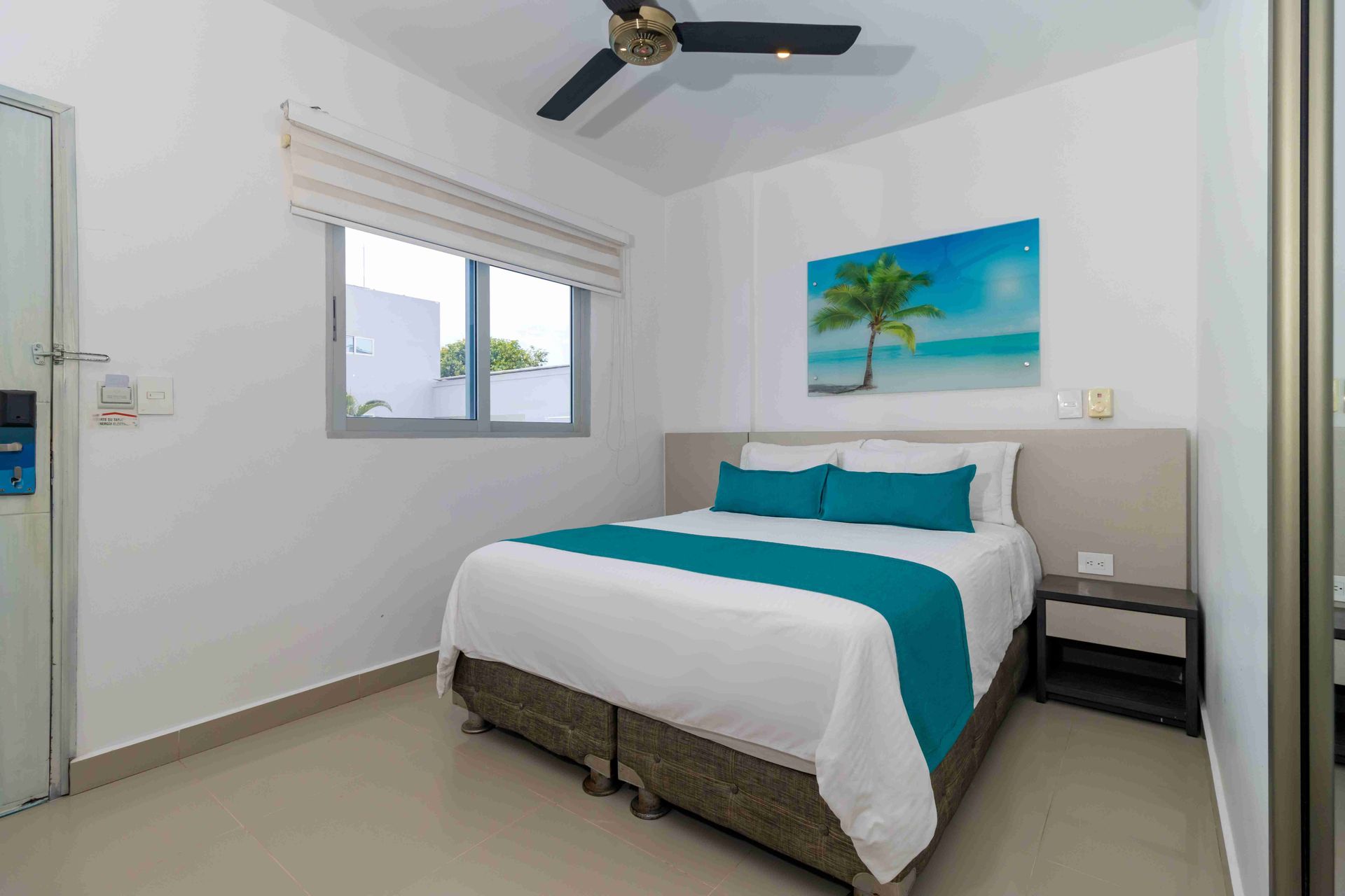 cama matrimonial, ventilador negro en el techo y decoración tropical en habitaciones en coveñas