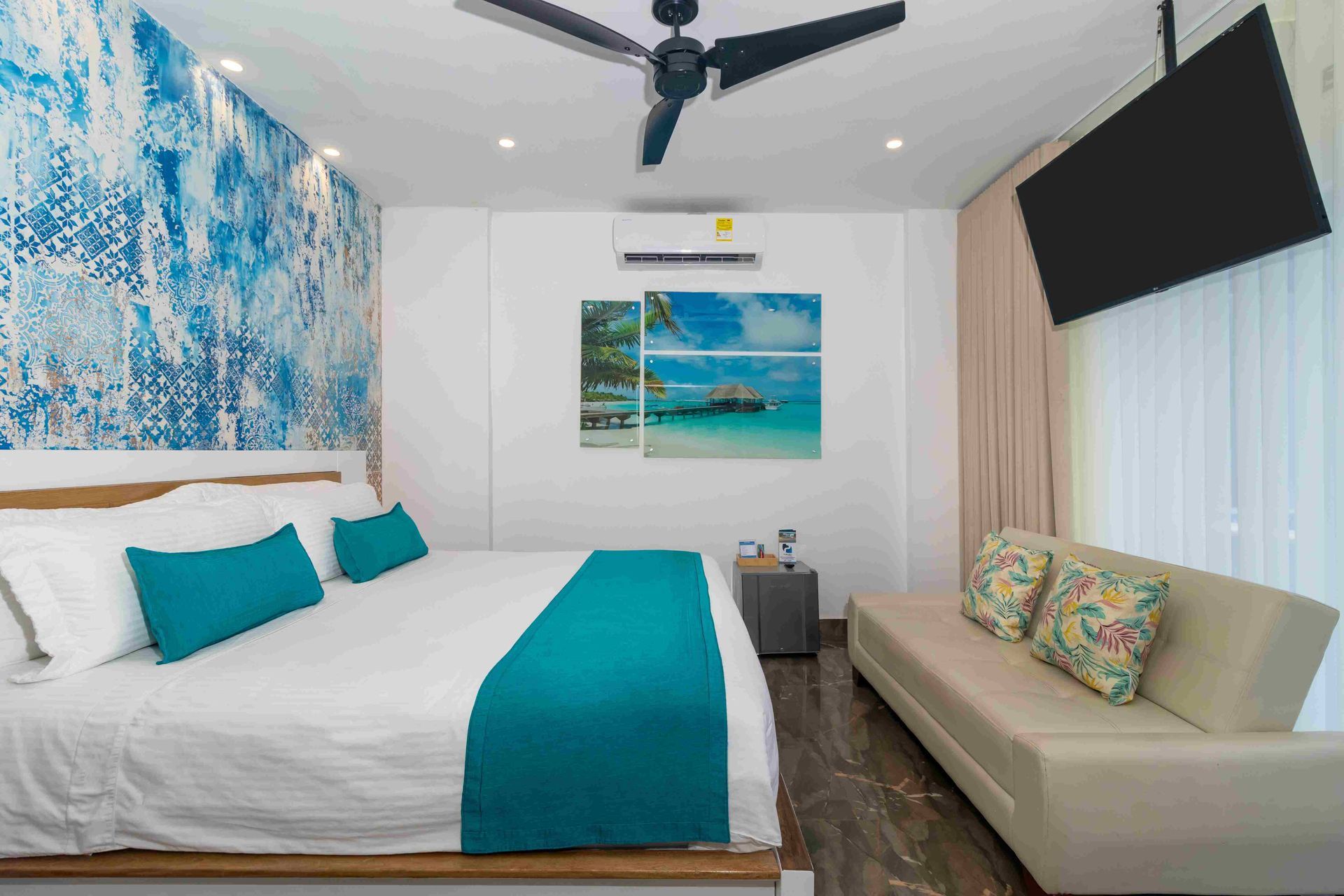 habitaciones en coveñas en Hotel Poblado con cama matrimonial, sofá, televistor y decoración de pared en tonos azules