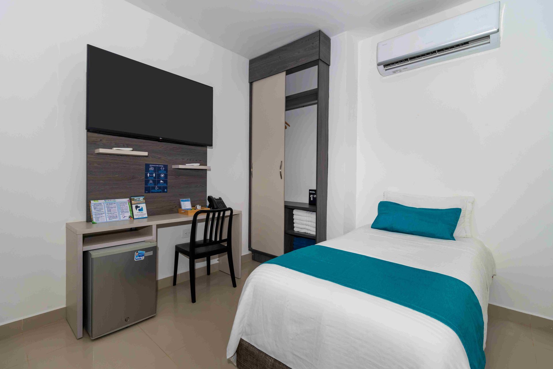 Habitación en Hotel Poblado Coveñas con cama sencilla, televisor, escritorio, armario y aire acondicionado