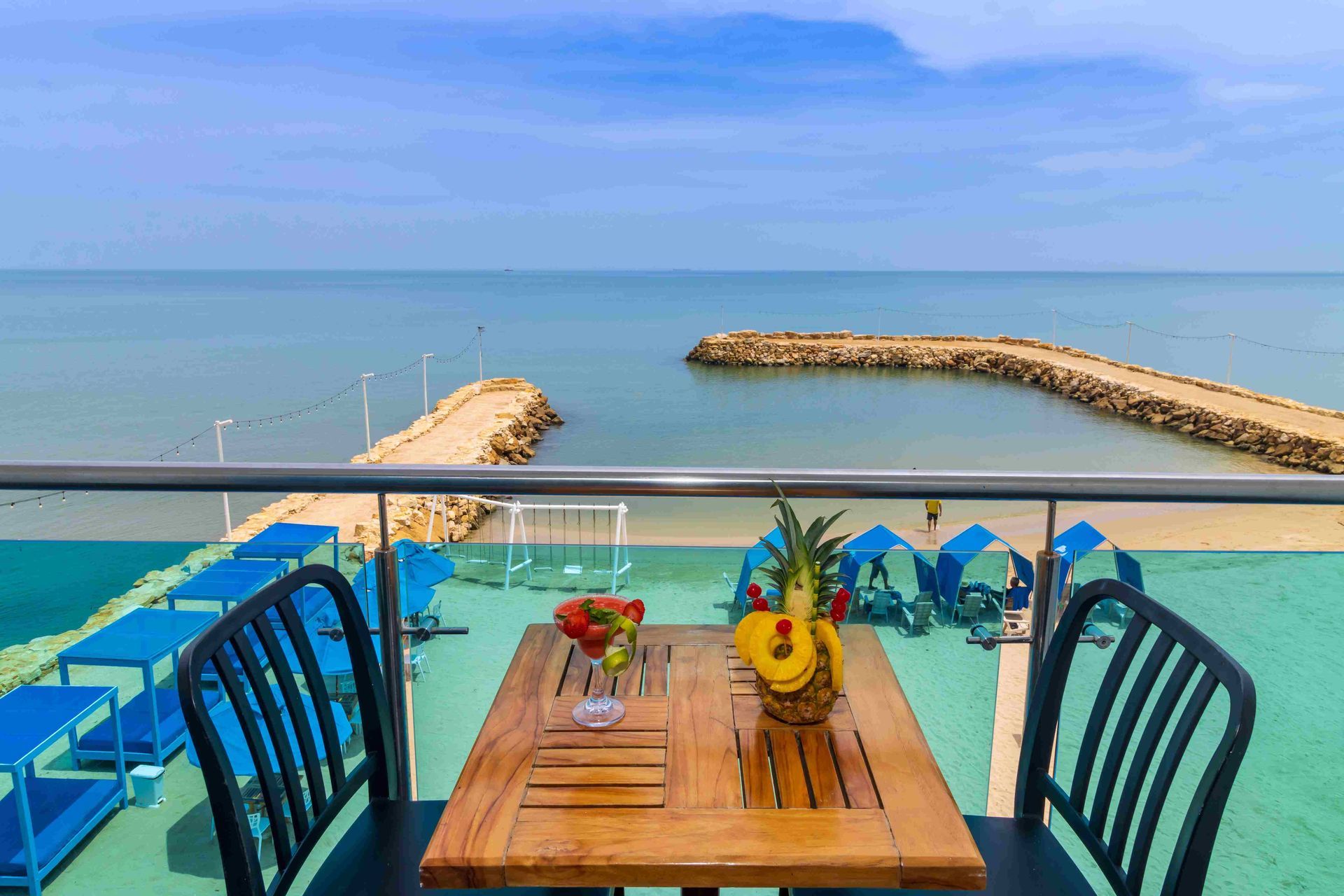 Mesa de madera y sillas negras en un balcón con baranda de vidrio, ideal para disfrutar un hotel en coveñas con vista al mar