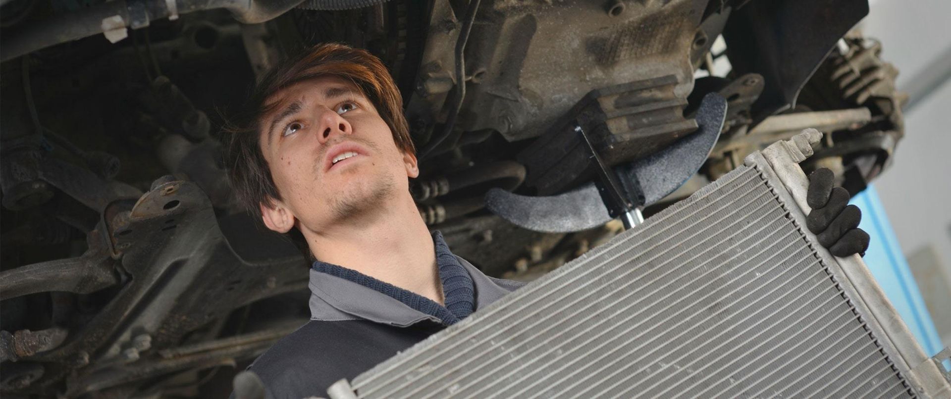 Un hombre sostiene un radiador debajo de un coche.