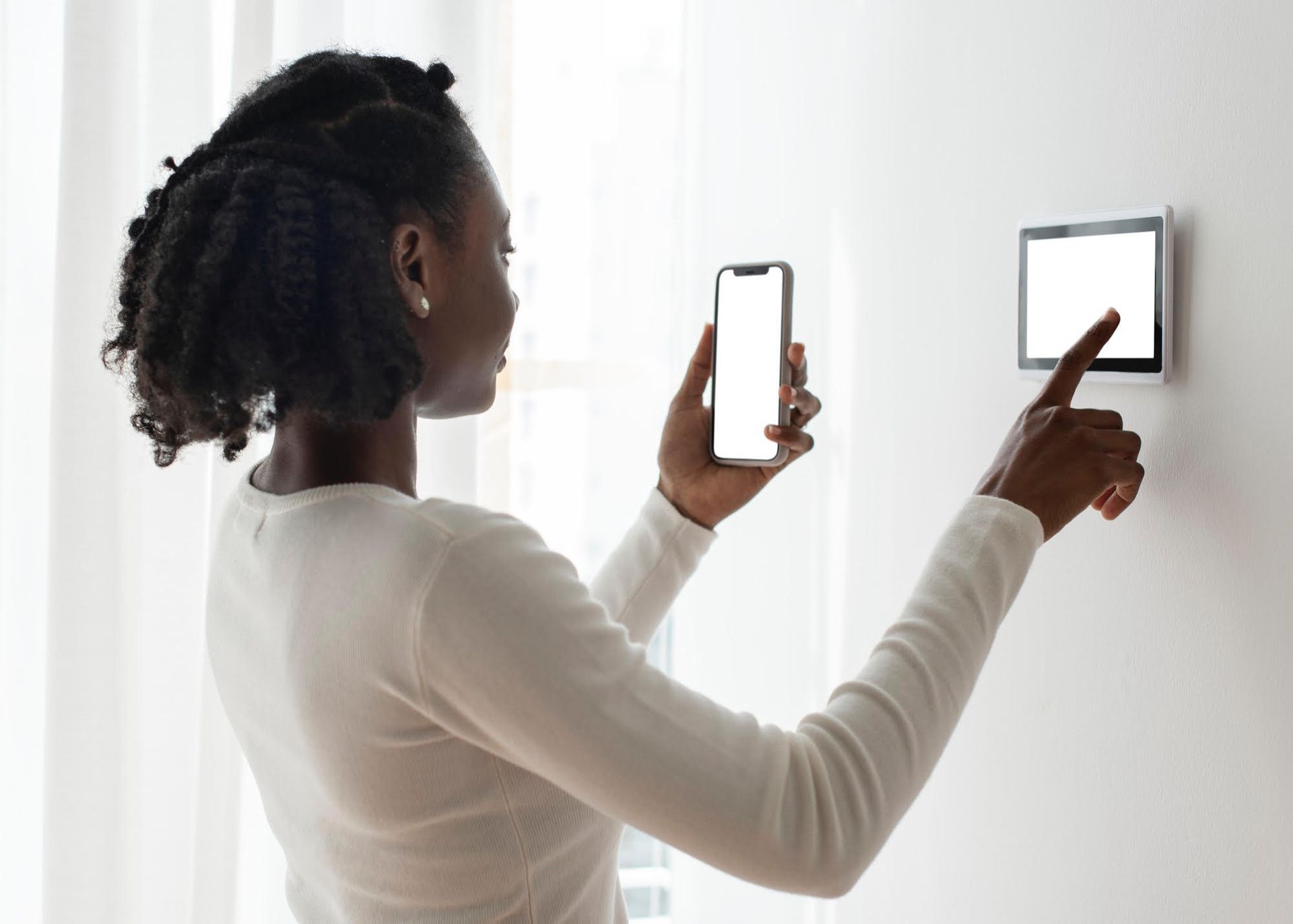 A woman is using a smart phone to control a thermostat.