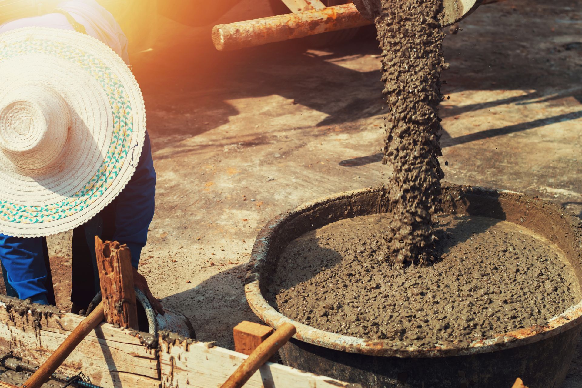 Construction worker mixing wet cement in wheelbarrow at job site during concrete work outdoors labor.