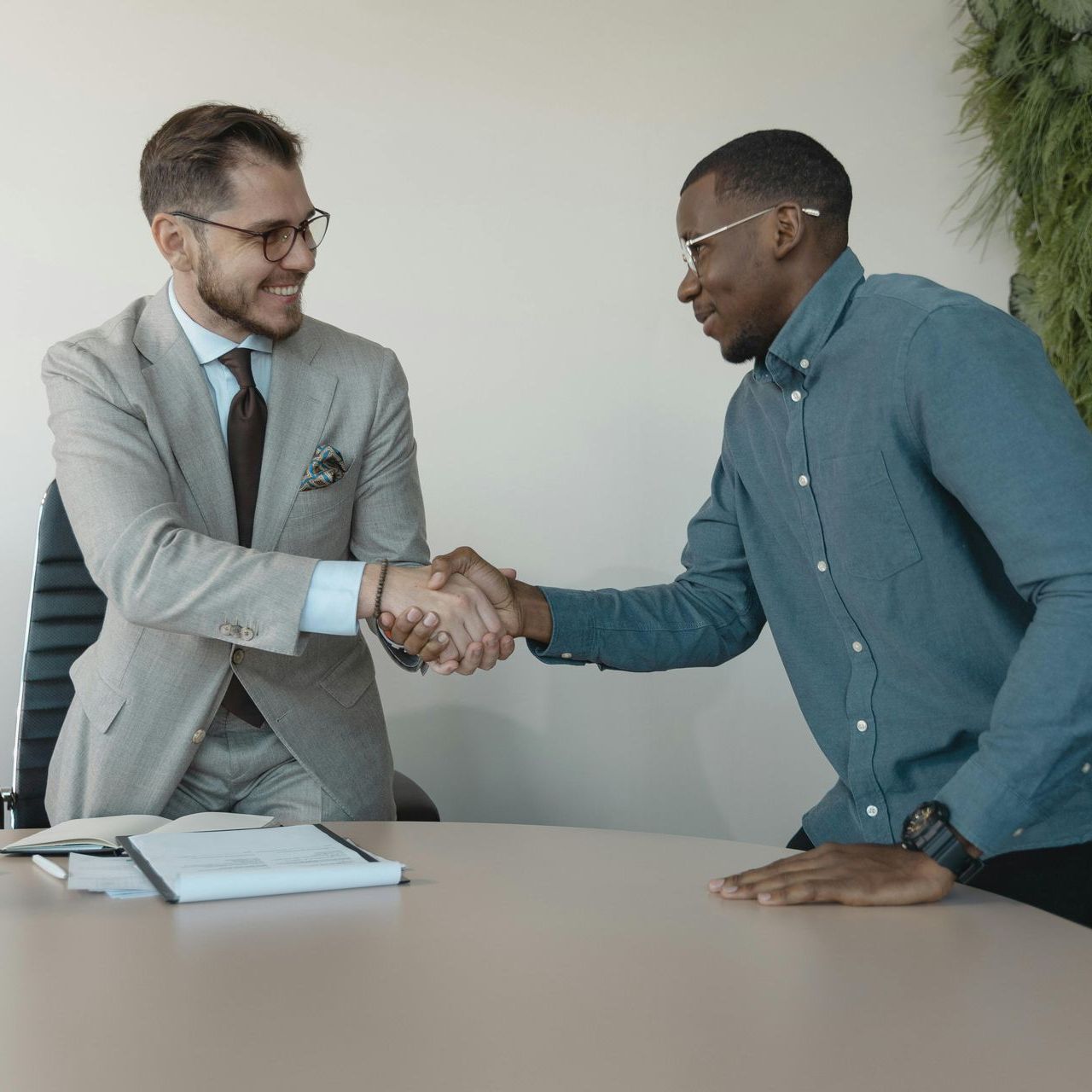 Two men shaking hands while sitting at a table