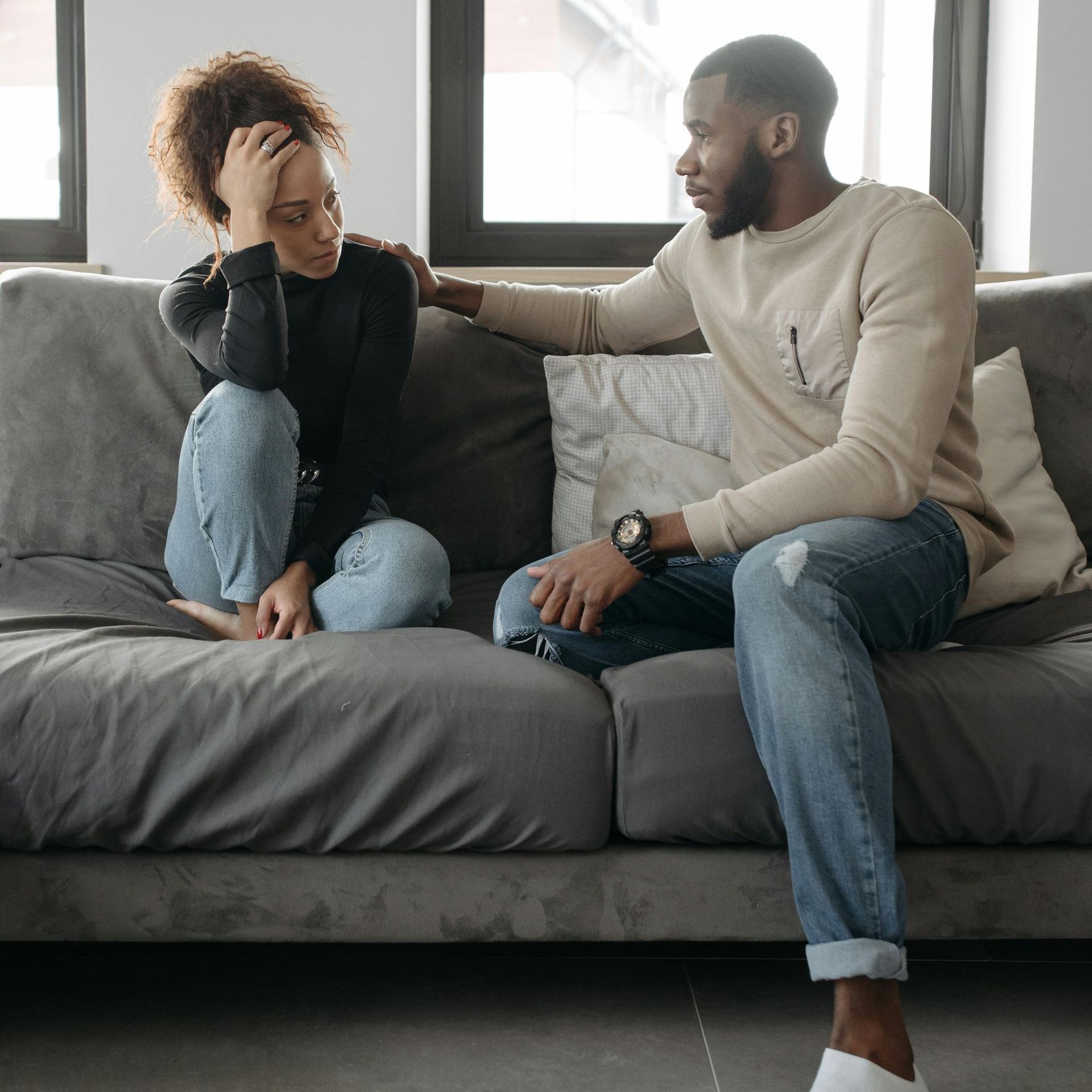 A man and a woman are sitting on a couch talking to each other.