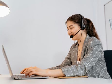 A woman wearing headphones is sitting at a desk using a laptop computer.