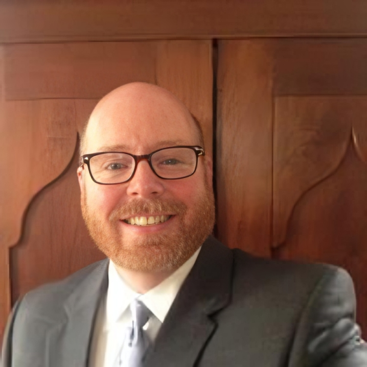 Bald man with glasses and red beard, wearing a suit, smiling.