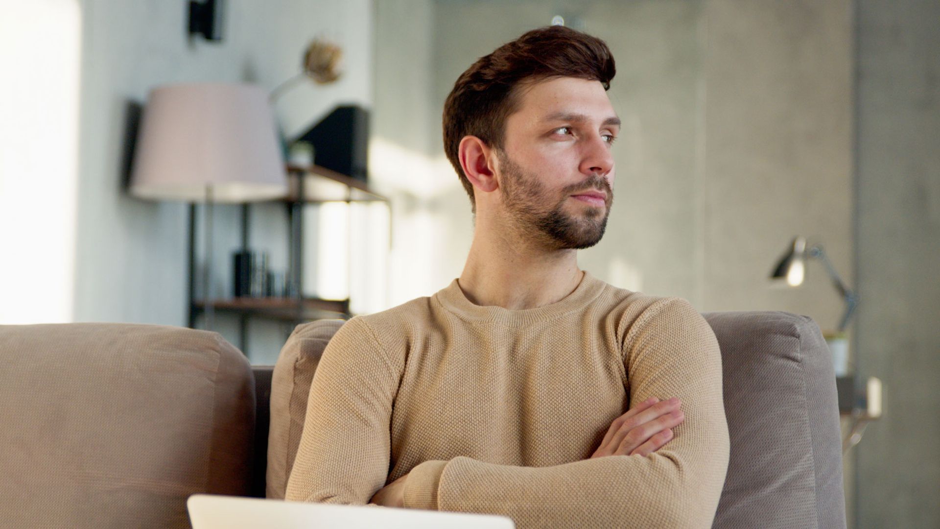 Upset adult man sitting on couch with computer open
