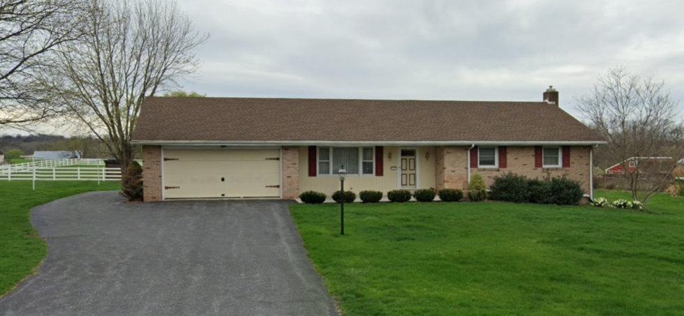 Single-story brick house with attached garage, dark roof, and a curved driveway under overcast skies
