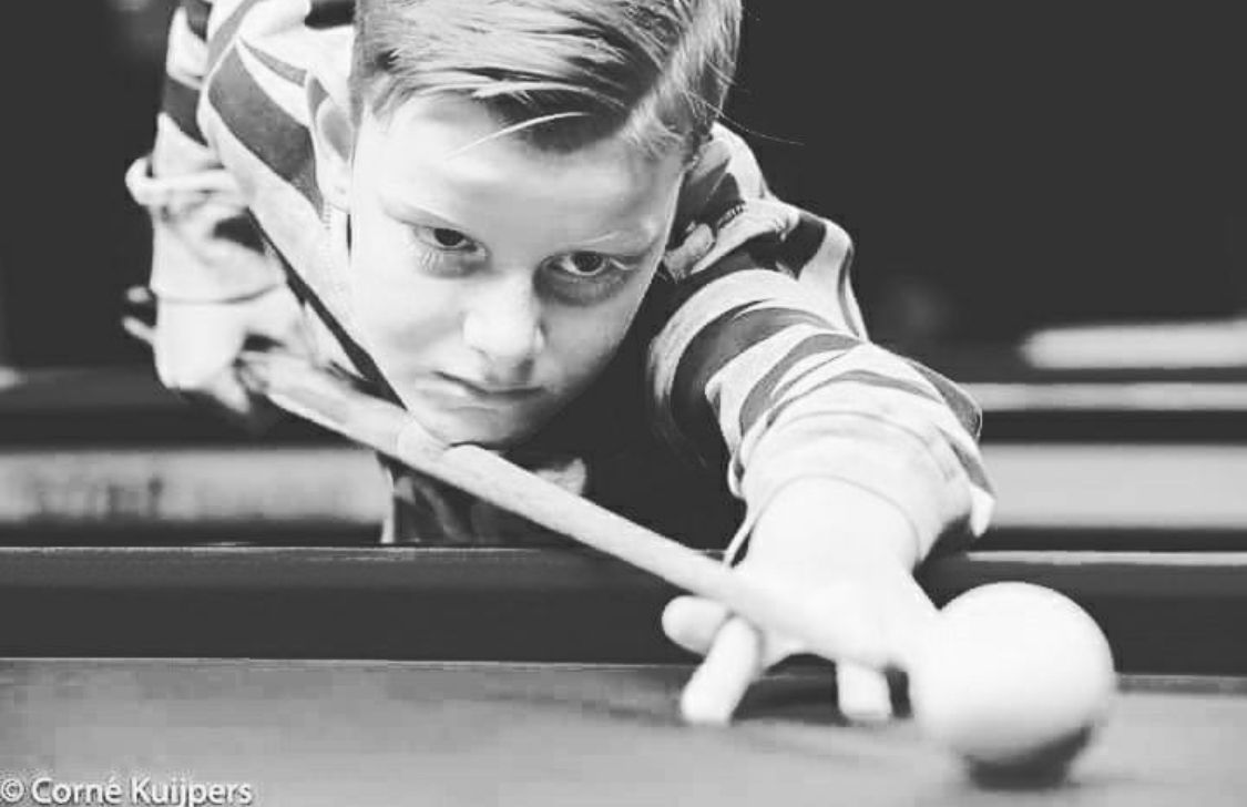 Jongen richt aandachtig zijn keu op een biljartbal op een pooltafel.