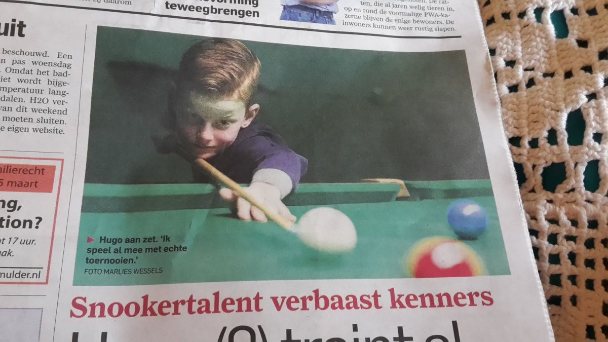 Boy playing snooker, aiming cue stick at white ball. Green table, other balls present.