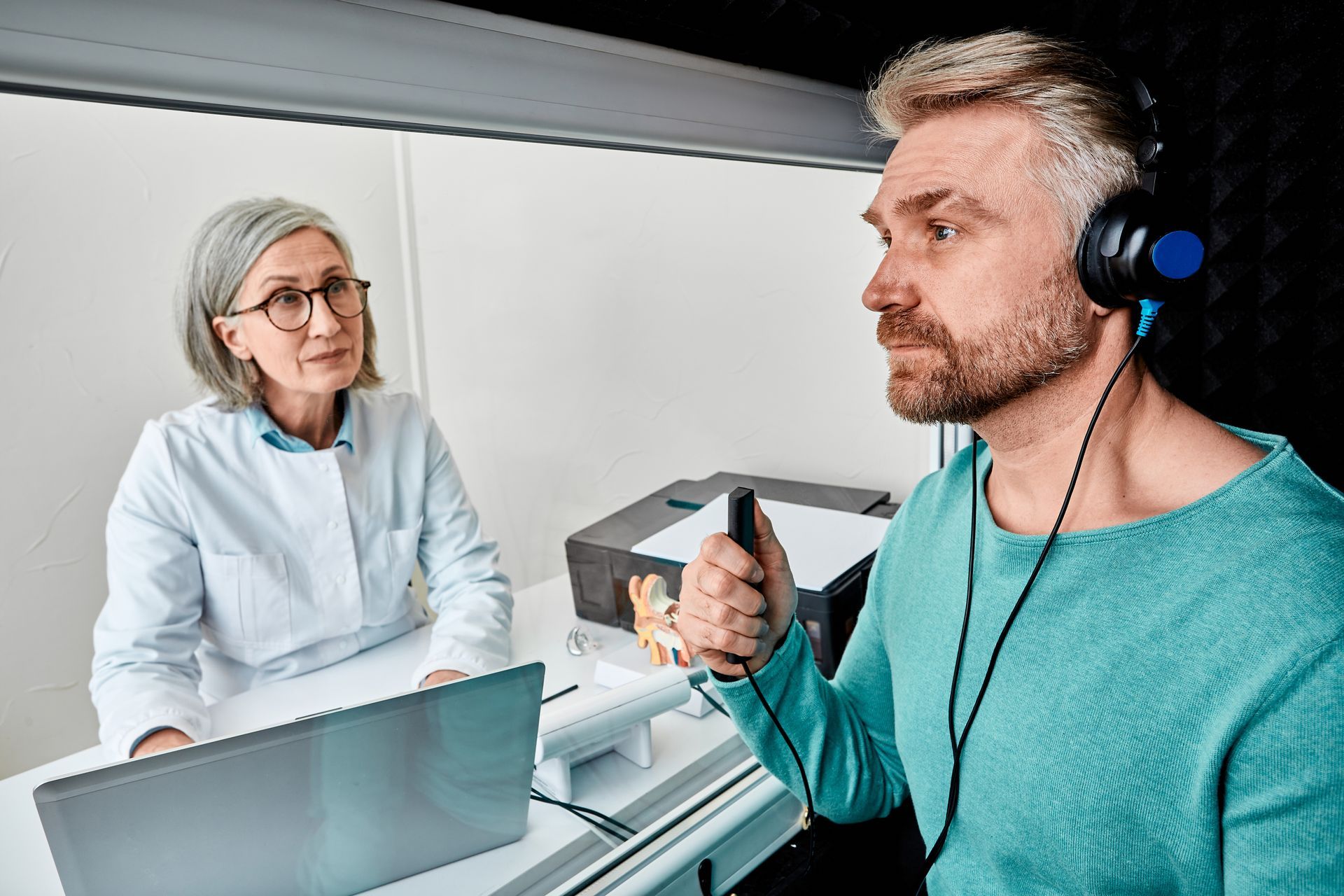 Man wearing headphones taking a hearing test. A healthcare provider observes.