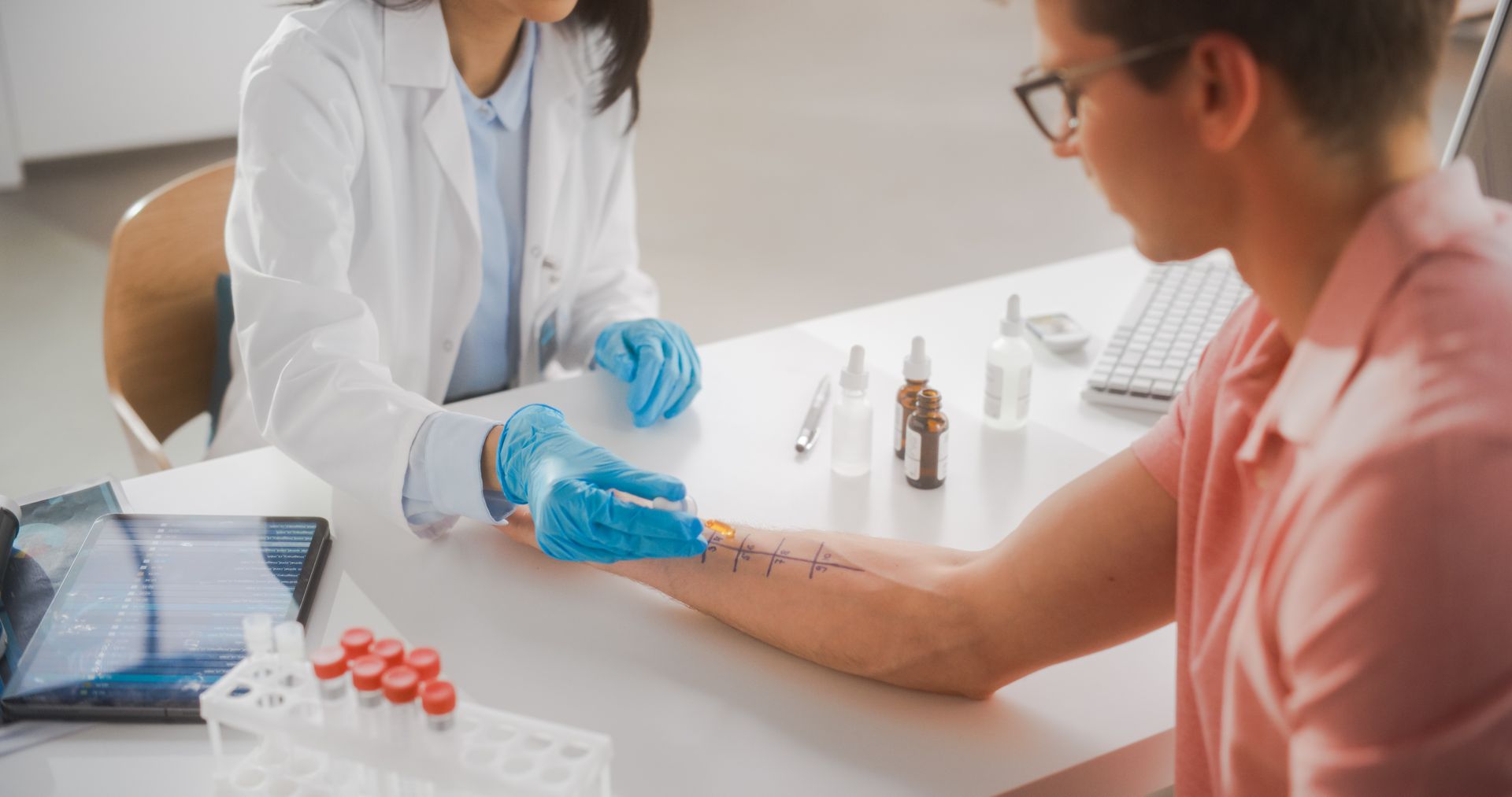 Doctor performs allergy skin tests on a patient's forearm at a desk in a clinic.