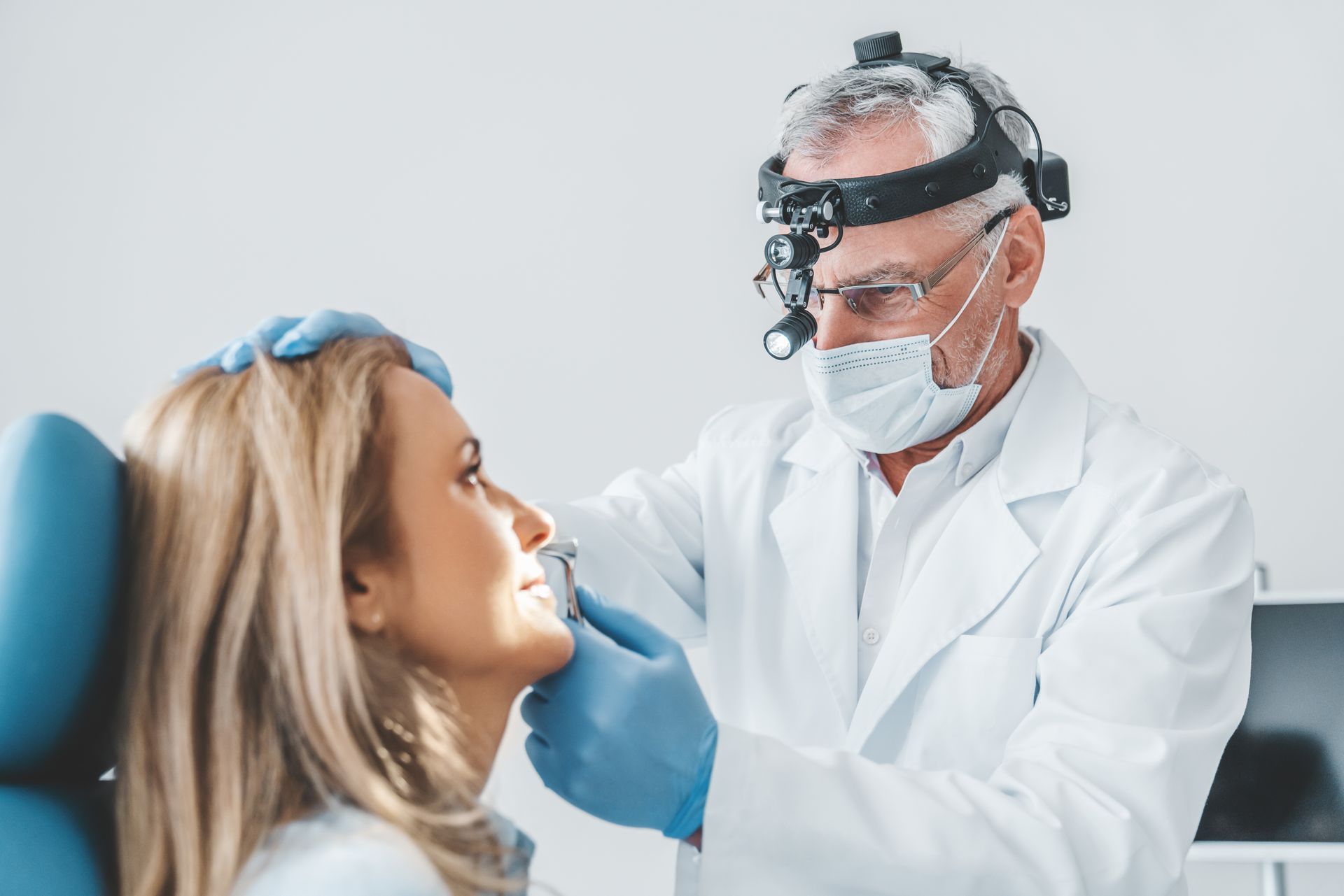 Doctor examining a patient's nose with a headlamp in a medical office.