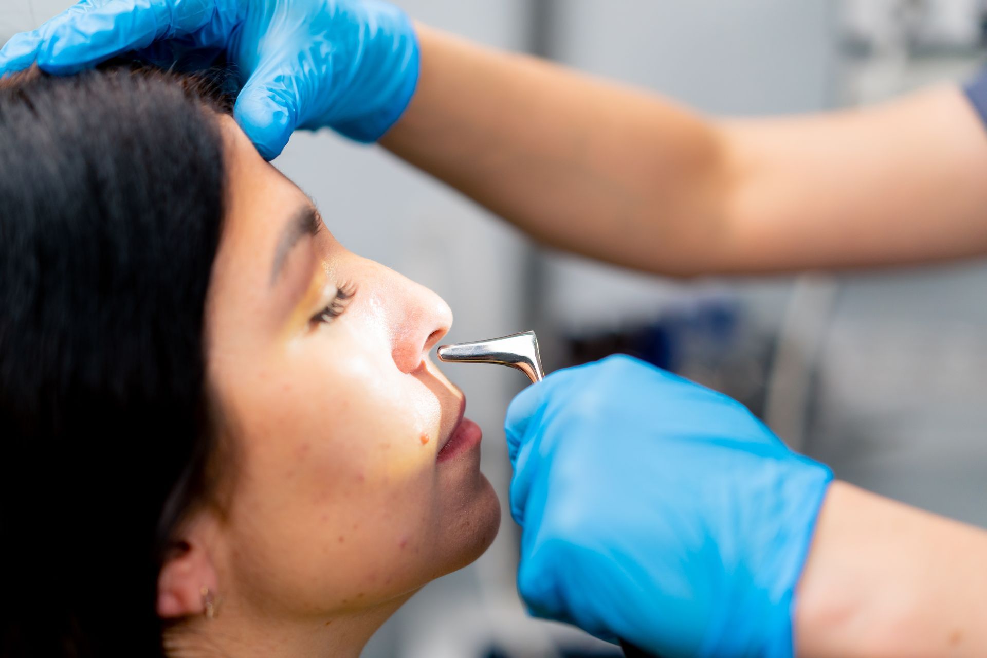 Person receiving a nasal examination by a medical professional wearing blue gloves.