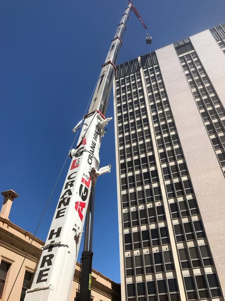 A large crane lifting materials up to a building under a blue sky — Adelaide, SA — AGL & Son Crane Hire