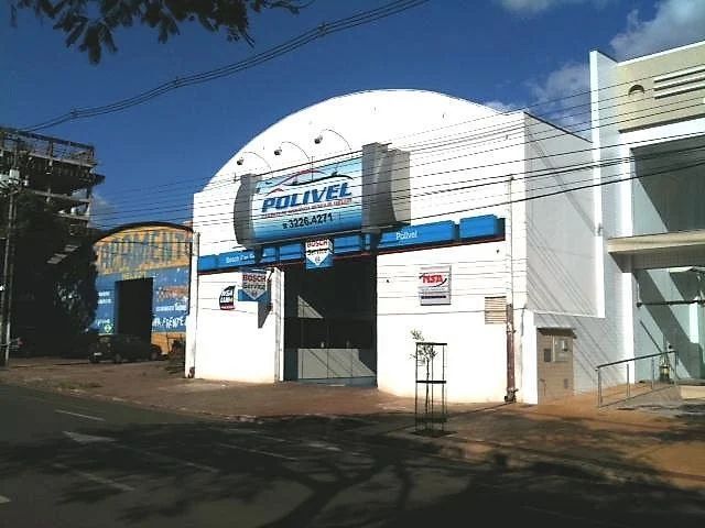 Vista ao nível da rua da oficina da Polivel, apresentando uma grande fachada arqueada e uma área de serviço aberta.