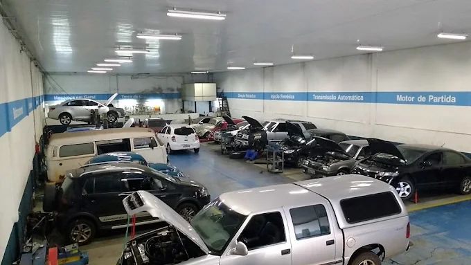 Oficina mecânica com vários carros estacionados no interior, alguns com os capôs ​​abertos, sob uma forte iluminação no teto.