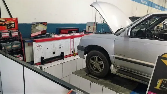Carro prateado com o capô aberto em um elevador dentro de uma oficina mecânica, com equipamentos de diagnóstico visíveis.