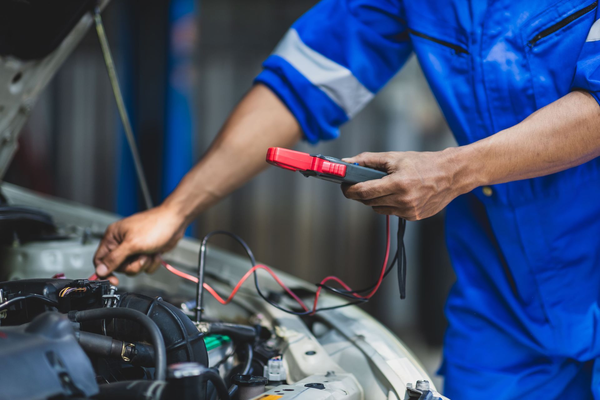 Um mecânico de macacão azul usa um multímetro para testar os componentes elétricos do motor de um carro.